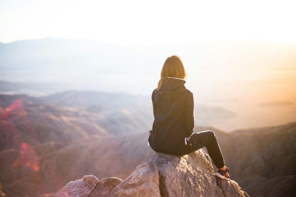 person sitting on top of gray rock overlooking mountain during daytime- dealing with doubt